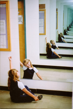 A picture of a girl looking into a mirror, opposite another mirror, forming an infinite cooridor of reflections. This is a visual example of recursion. The nested instances of the reflection are the recursive case. The fade to dark green is the base case.